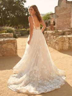 a woman in a wedding dress is standing on the dirt road near an old building