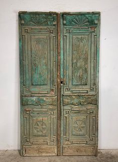 an old green wooden door with carvings on the front and side doors, in a white walled room