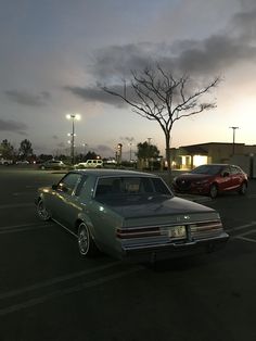 two cars are parked in a parking lot at dusk, one is green and the other is red