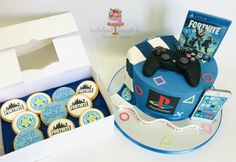 a decorated cake and some cookies with video game controllers on it, next to a box of cookies