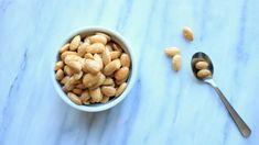 a white bowl filled with peanuts next to a spoon