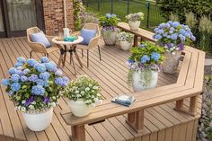 a wooden deck with potted plants and chairs on it, next to a table