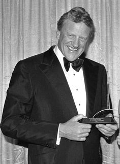 a man in a tuxedo smiles while holding an award