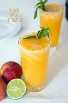 two glasses filled with orange juice and garnish next to fruit on a table