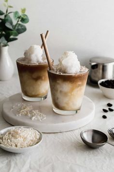 two glasses filled with ice cream sitting on top of a white table next to spoons