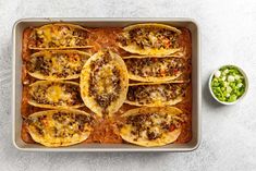 an overhead view of some tacos in a pan with salsa and green onions on the side