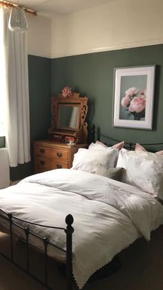 a bed with white linens and pillows in a green room next to a dresser