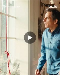 a man standing in front of a window next to a christmas tree