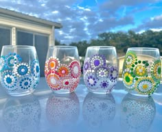 four wine glasses with different designs on them sitting in front of a window sill