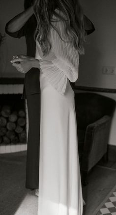 a woman in a long white dress standing next to a couch