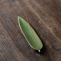 a green leaf sitting on top of a wooden table next to a pair of needles