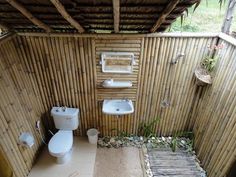 an outdoor bathroom with bamboo walls and flooring, toilet and bidet in the corner