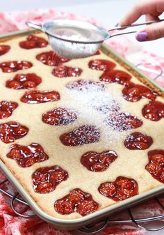 a person scooping sugar into a pan filled with heart shaped pastries on a red and white table cloth