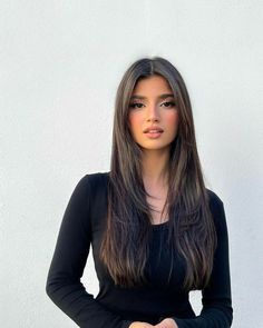 a woman with long hair standing in front of a white wall wearing a black top