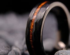 a wedding band with an orange and black wood inlay is on top of some rocks