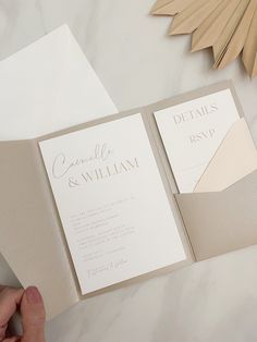 a person holding an open wedding card in front of a white and beige pocketfold