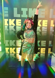 a woman in a sequin dress and black blazer posing for the camera with her hands up