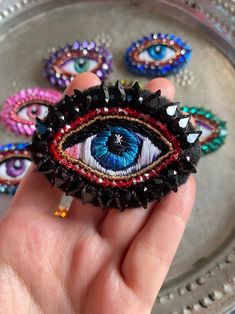 a hand holding an evil eye broochle on top of a metal platter