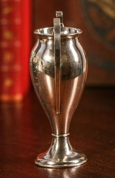 a silver vase sitting on top of a wooden table next to a red bookcase