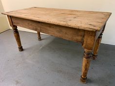 an old wooden table sitting on top of a cement floor next to a white wall