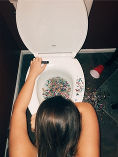 a woman sitting on top of a white toilet bowl filled with confetti and sprinkles