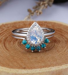 an engagement ring with a pear shaped diamond surrounded by turquoise stones on a wooden stand