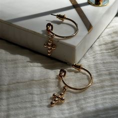 CROSS DROP HOOP EARRINGS IN GOLD SHADE These Cross Drop Hoop Earrings in an elegant gold shade beautifully merge the classic charm of the Old Money aesthetic with a touch of modern coquette flair. The perfect gift for her, these earrings are both stylish and meaningful, featuring a dainty cross pendant that dangles gracefully from sleek hoops. Ideal for adding a sophisticated statement to any outfit, these earrings blend the timeless appeal of hoop earrings with the spiritual symbolism of cross Trendy Gold Dangle Hoop Earrings, Dainty Metal Dangle Hoop Earrings, Trendy Dangle Hoop Earrings In Brass, Trendy Brass Dangle Hoop Earrings, Trendy Gold Hoop Earrings With Dangling Charms, Adjustable Gold Earrings With Dangling Charms, Gold Earrings With Dangling Charms, Trendy Gold Earrings With Dangling Charms, Metal Hoop Earrings With Dangling Charms For Gift