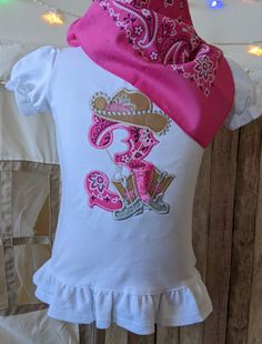 Fun cowgirl birthday shirt has bandana print fabric for the appliqued number hat and boots are faux suede and contrast fabric. Boots have fluffy fringe on backs. Shirt is a 100% white tee with puffed sleeves and a short ruffle on bottom edge. Care Instructions:  Wash in cold water. No bleach. Hang or tumble dry on low; do not iron directly over design. Returns/Refunds:  On custom orders, we cannot accept returns or refunds. Refunds will only be issued if we have made an error in the customizatio White Cotton Top For Country Events, White Cotton Tops For Country Events, 21st Birthday Shirts Cowgirl, White Cotton Tops With Bandana Print, White Cotton Top With Bandana Print, Cowgirl Themed Birthday Shirt, Horse Birthday Party Shirt, Pink Barnyard Birthday Shirt, Fluffy Fringe