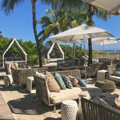 an outdoor seating area with umbrellas, chairs and tables on the sand near palm trees