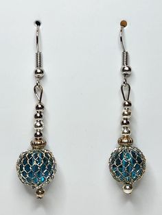 two pairs of blue and silver earrings on a white surface, one is dangling from a hook