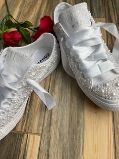 two pairs of white shoes with bows and pearls on the soles are sitting on a wood floor