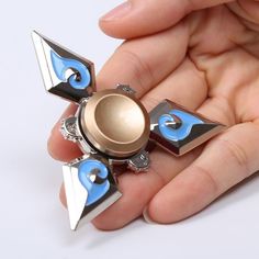 a hand holding a small metal object with blue and white designs on it's sides