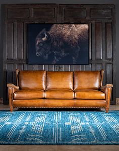 a brown leather couch sitting in front of a painting on the wall next to a blue rug