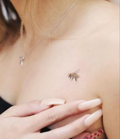 a woman's chest with a small bee tattoo on it, and her hand