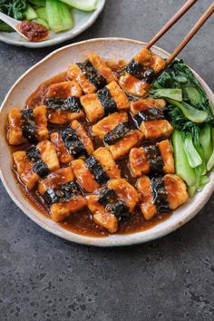 tofu and greens in a bowl with chopsticks resting on the plate next to it