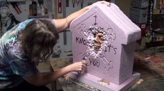 a woman is decorating a pink memorial in the shape of a house with flowers on it