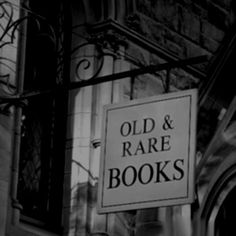 an old and rare book store sign hanging off the side of a building in black and white