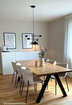 a dining room table with white chairs and a vase on it's end, in front of a window