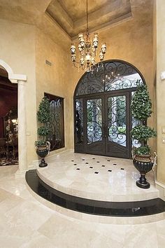 a large foyer with chandelier and two planters on the steps leading to it