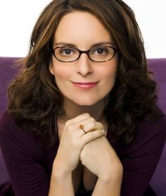 a woman wearing glasses sitting on a purple couch with her hand under her chin and looking at the camera