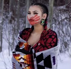 a woman with painted face standing in front of snow covered trees and holding onto a scarf