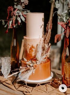 a three tiered cake sitting on top of a wooden table next to bottles and flowers