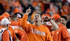 an orange shirted clemson football player is pointing to the sky with his team mates