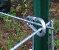 a close up of a chain link on a green pole with grass and trees in the background