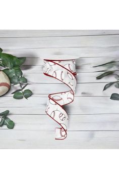 the baseball ribbon is next to some green leaves and a ball on a white wooden surface