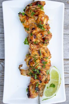 chicken skewers on a white plate with a lime wedge next to it and a slice of lime