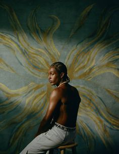 a woman sitting on top of a stool in front of a wallpapered background