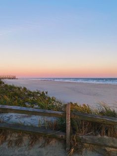 an empty beach at sunset with the ocean in the back ground and sand dunes to the side