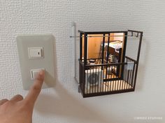 a hand is pointing at an electrical outlet with a cage on the wall above it