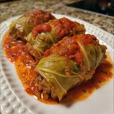 cabbage stuffed with meat and marinara sauce on a white plate in front of a granite countertop